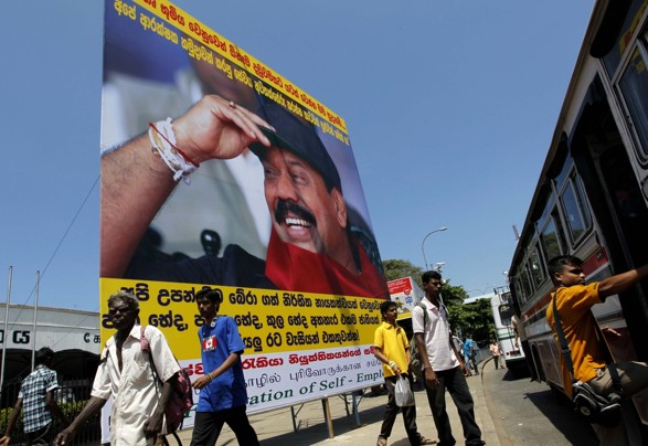Sri Lankans walk past a billboard of President Mahinda Rajapaksa and campaign slogans for people to join the protest against the U.N. report, Colombo, Apr 21 2011